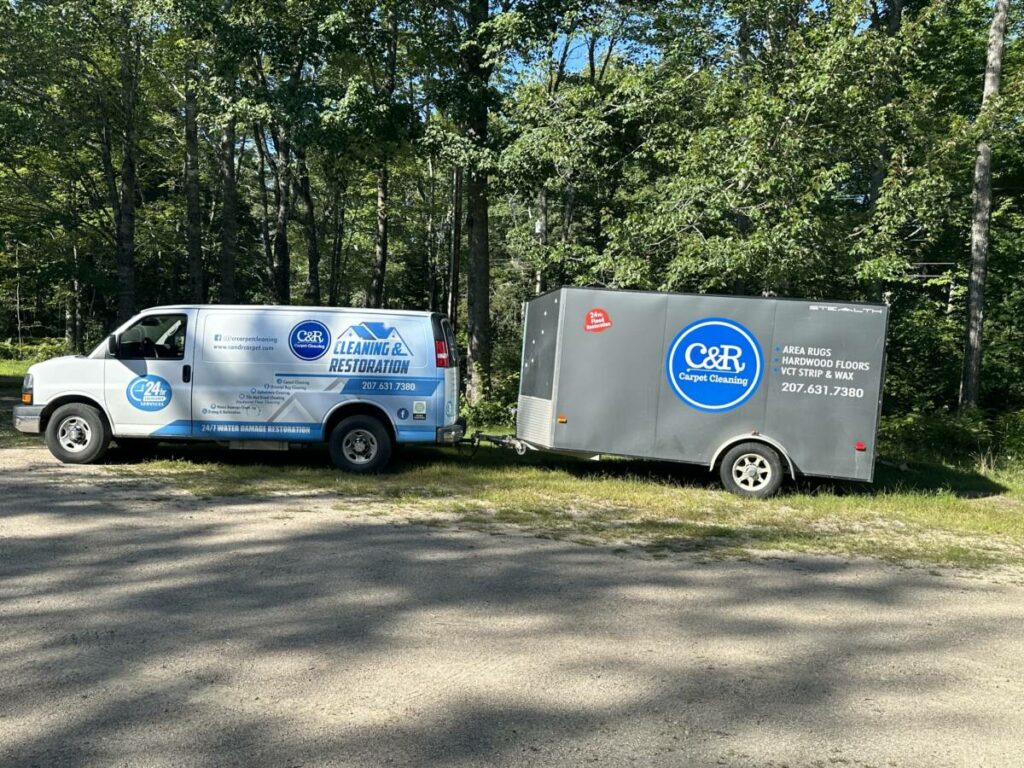 C&R cleaning and restoration van with a gray equipment trailer parked at the edge of the woods